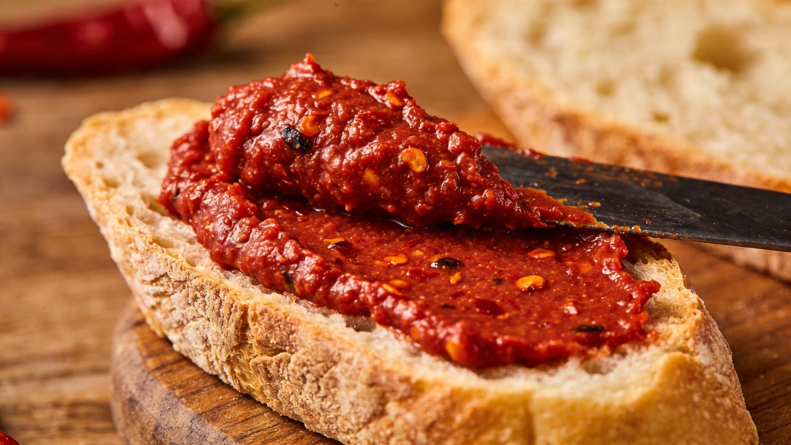 A close-up of vibrant, crimson 'nduja being spread onto rustic bread, showing its rich, fatty texture and flecks of Calabrian chili.