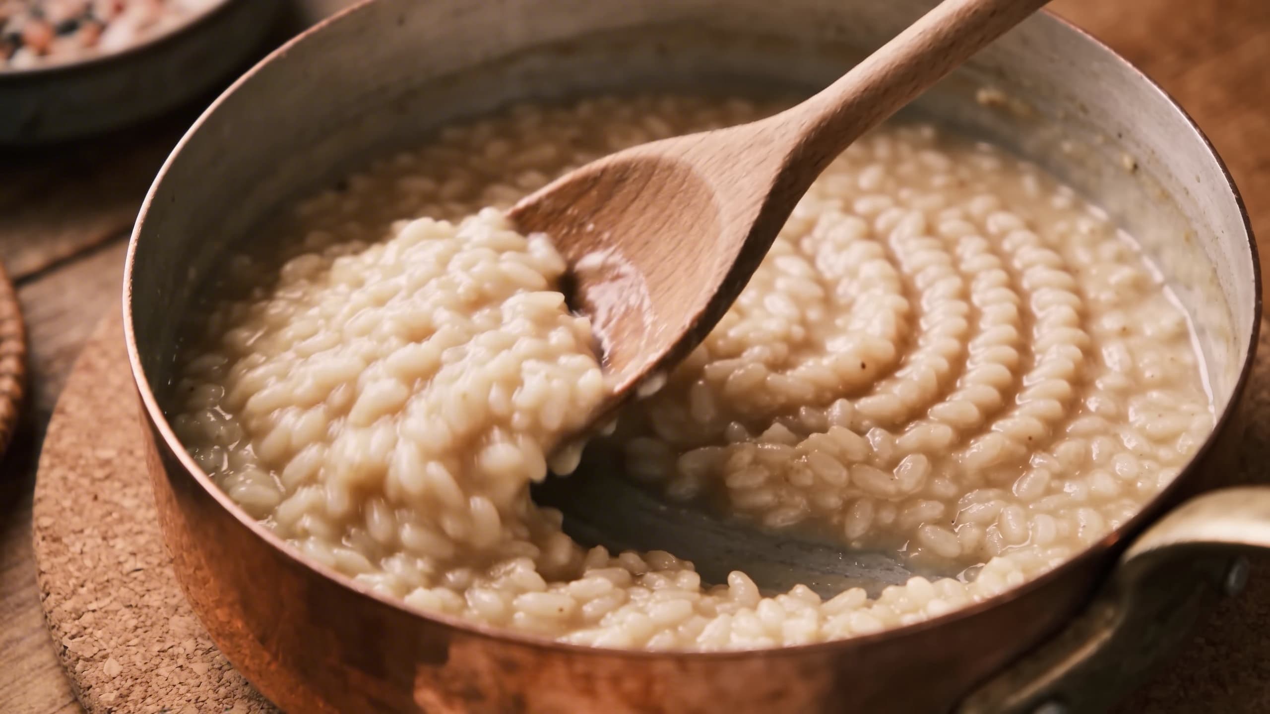 A step-by-step demonstration of the "Mantecatura" stirring technique, showing the rhythmic movement of the wooden spoon creating a creamy emulsion.