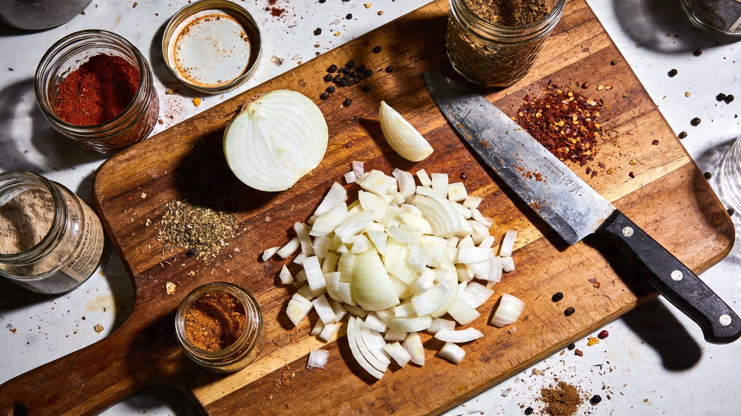 A chaotic kitchen counter with open spice jars, half-chopped onions, and a cluttered workspace.