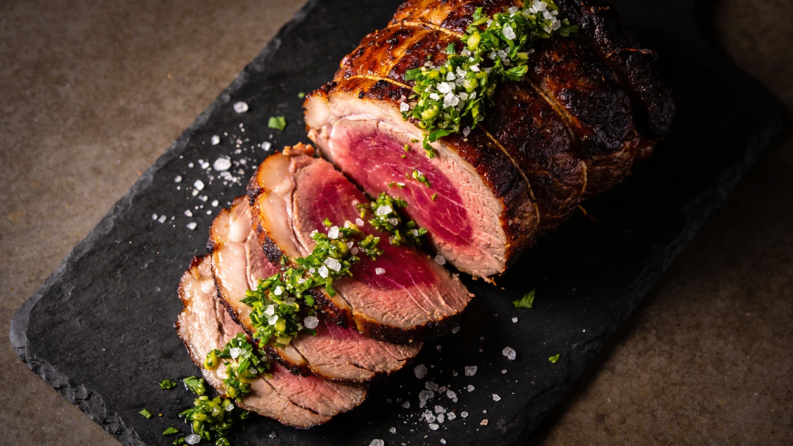 A professional plating of a smoked rump roast, sliced thin to show a perfect smoke ring, garnished with fresh, vibrant green gremolata.